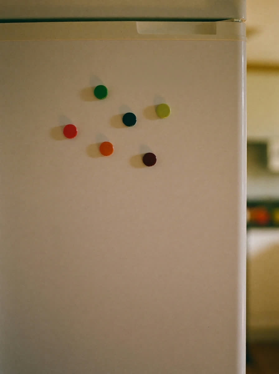 A cream refrigerator door in morning light with a handwritten note taped to it
